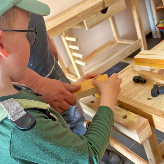 Kind arbeitet mit Unterstützung einer erwachsenen Begleitperson an einem Holzstück im Werkkurs in Köln