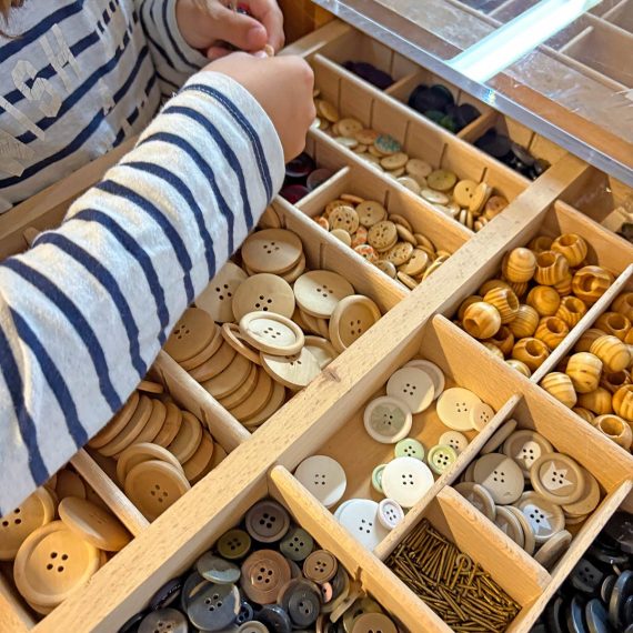 Kind gestaltet mit Knöpfen und kreativen Materialien im Familienkurs der Kölner Kinderwerkstatt in Köln.