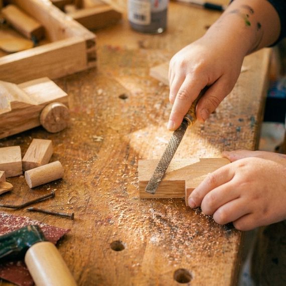 Kind bearbeitet Holz mit einer Feile im Sommerferienkurs Werken und Gestalten der Kölner Kinderwerkstatt in Köln.