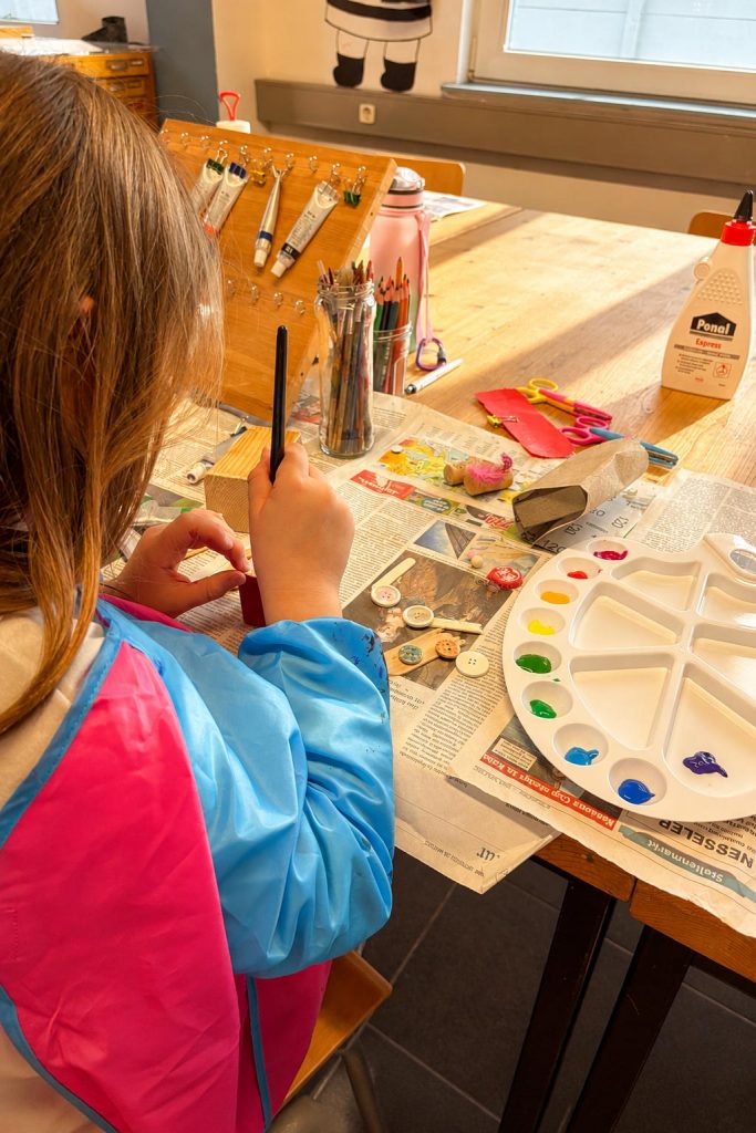 Kind gestaltet mit Farben, Pinseln und verschiedenen Materialien im Kurs Malen & Zeichnen der Kölner Kinderwerkstatt in Köln