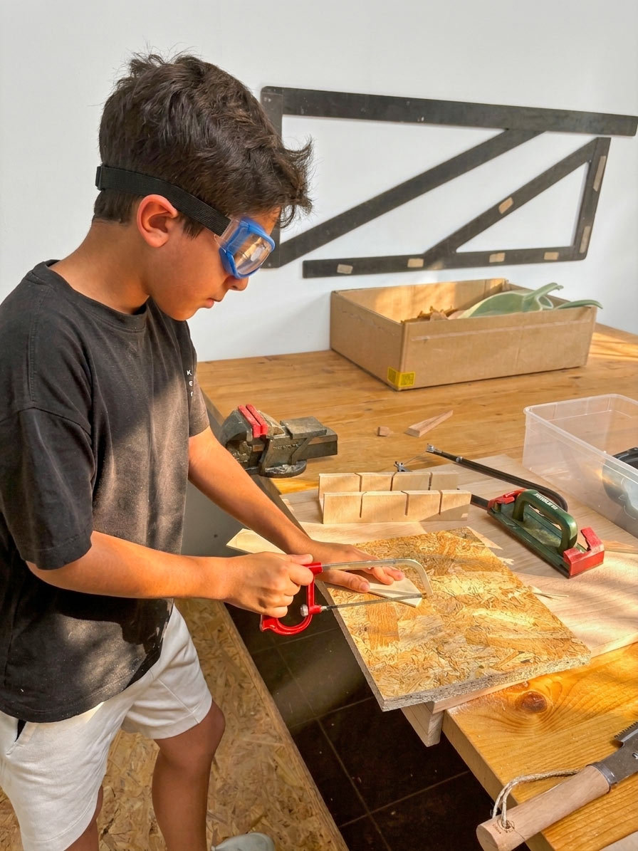 Kind sägt mit Schutzbrille ein Holzstück im Kurs Werken & Gestalten der Kölner Kinderwerkstatt in Köln