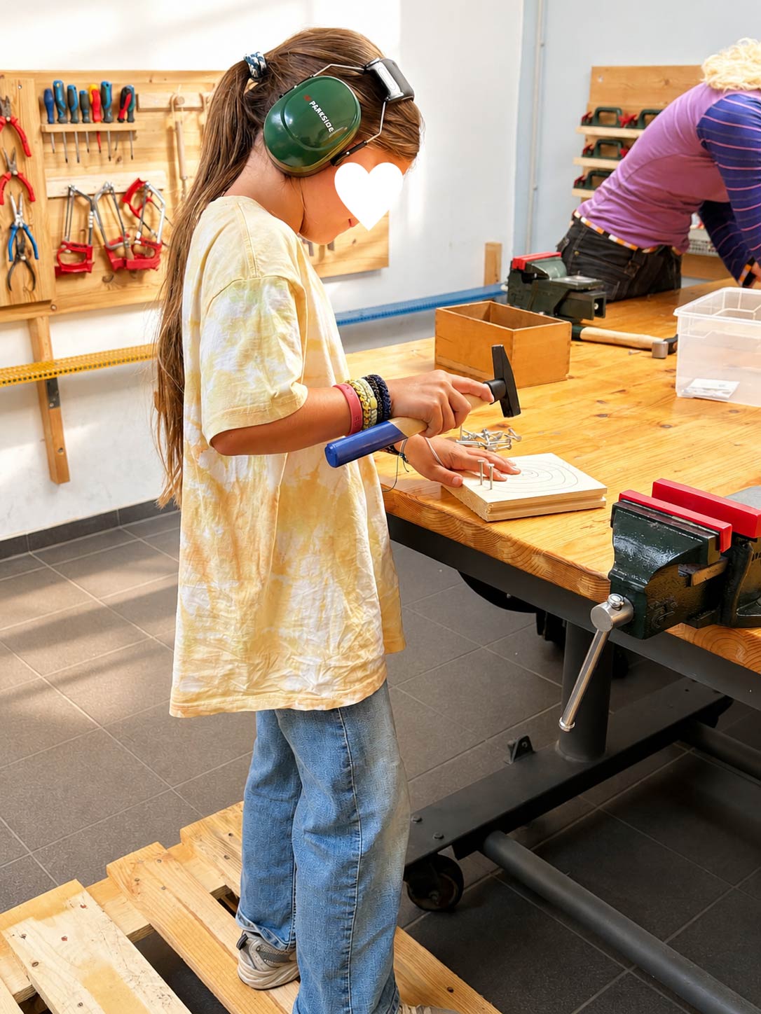Kind arbeitet mit Hammer und Gehörschutz an einem Holzprojekt im Herbstferienkurs Werken & Gestalten der Kölner Kinderwerkstatt
