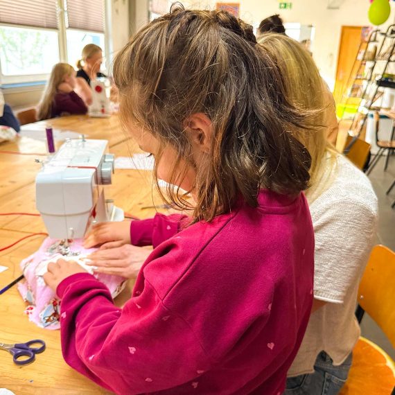 Kind näht gemeinsam mit einer Begleitperson an der Nähmaschine im Familienkurs der Kölner Kinderwerkstatt in Köln